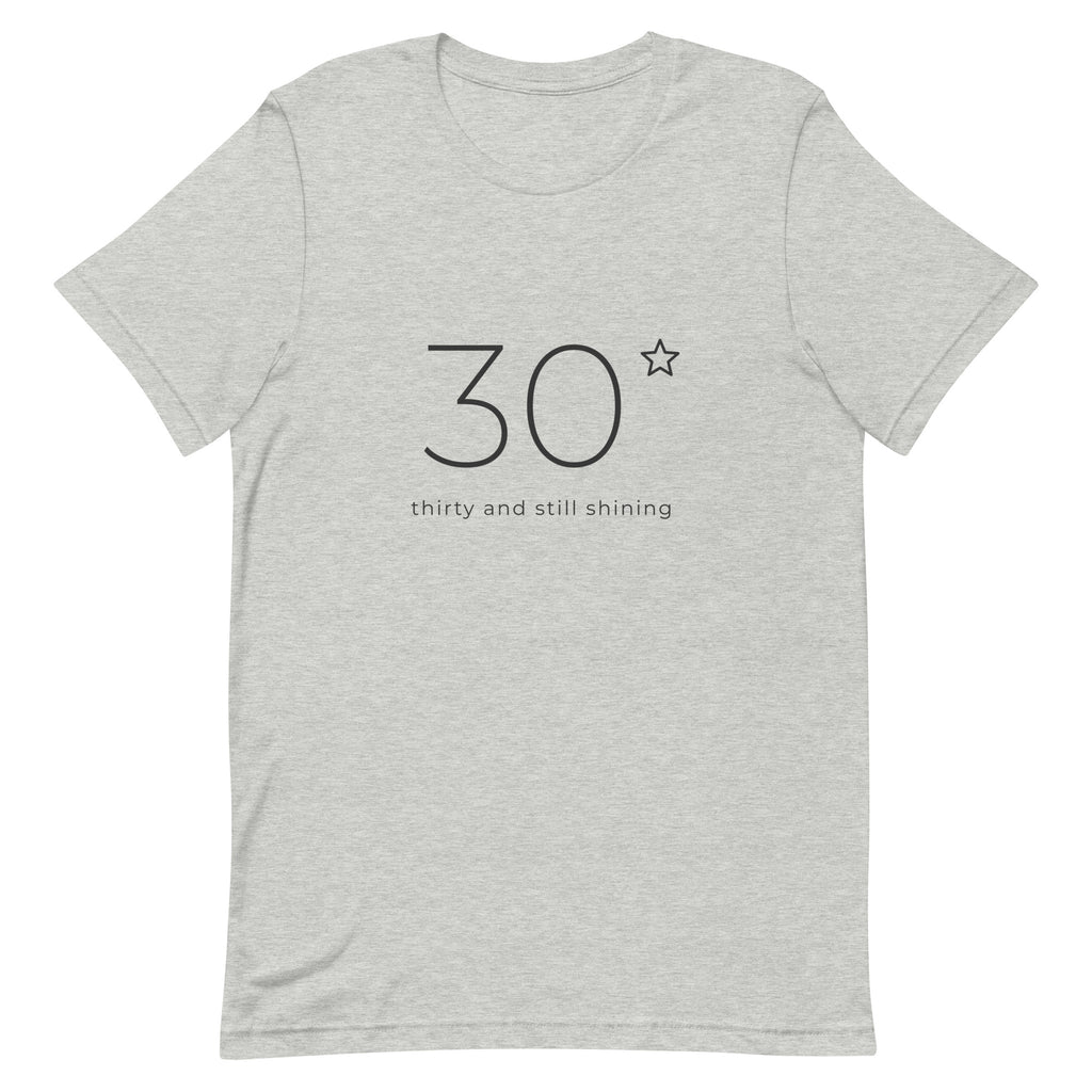 Front of the Thirty and Still Shining 30th birthday tee: a large fine line 30 with a small star and the words thirty and still shining, on a heather grey Classic Soft Tee